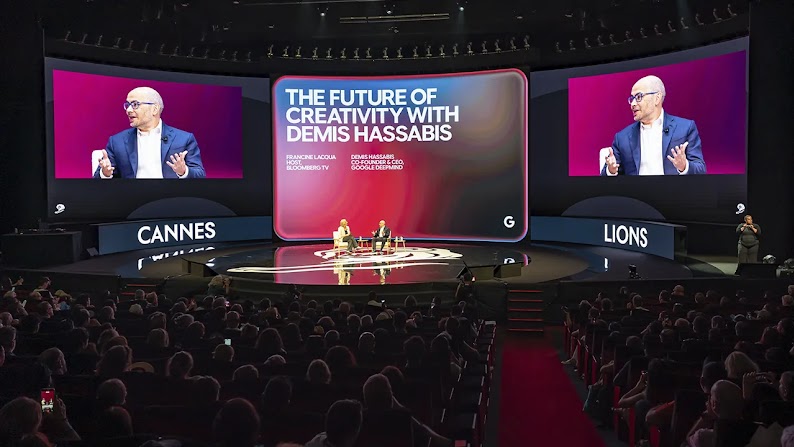 Francine Lacqua of Bloomberg TV interviews Demis Hassabis, CEO of Google DeepMind, on stage at the Cannes Lions Festival. Large screens behind them display Hassabis in close up and the title of the talk: The Future of Creativity with Demis Hassabis.