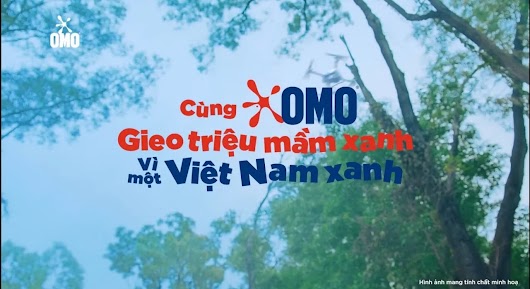 A promotional image for OMO featuring a low-angle view looking up at a bright blue sky surrounded by green tree branches. In the center, large stylized text reads "Cùng OMO Gieo triệu mầm xanh" in red, followed by "vì một Việt Nam xanh" in blue. The OMO logo appears in the top left corner and is integrated into the central text.