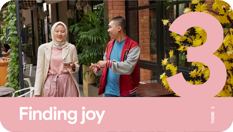 Theme 3: Finding joy. A woman and a man conversing as they walk along the outside of a well-decorated cafe.