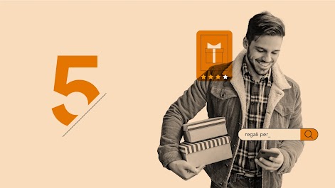 Una persona con una camicia di flanella e una giacca di velluto a coste tiene in mano 2 scatole decorative mentre usa uno smartphone per cercare regali.