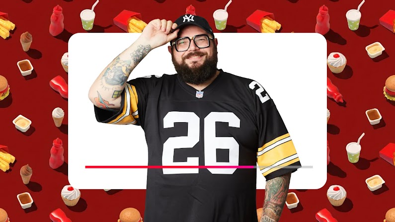 Mocho sorridente con cappellino nero, occhiali da vista, barba e maglia sportiva numero 26, posa su sfondo rosso decorato con vari elementi di fast food come hamburger, patatine e salse.