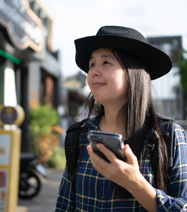 A woman wearing a hat is walking past a restaurant, phone in hand.