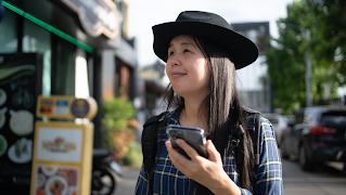 A woman wearing a hat is walking past a restaurant, phone in hand.