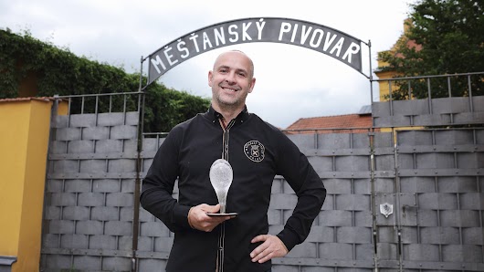 Ladislav Pártl, spolumajitel Měšťanského pivovaru Polná, stojí před bránou s nápisem Měšťasnký pivovar a drží ocenění Křišťálový špendlík.