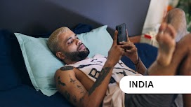 India. A man lying on his bed and using his phone to make travel plans.