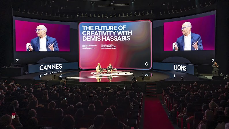 Francine Lacqua di Bloomberg TV intervista Demis Hassabis, CEO di Google DeepMind, sul palco del Festival di Cannes Lions. Grandi schermi dietro di loro mostrano Hassabis in primo piano e il titolo del discorso: Il futuro della creatività con Demis Hassabis.
