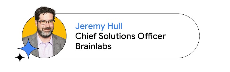 Jeremy Hull, Chief Solutions Officer at Brainlabs appears inside a yellow circle, wearing glasses, a gray jacket and a collared shirt. Hull has light skin, dark brown hair, and a graying beard. Blue sparkles appear in the bottom left of the photo.
