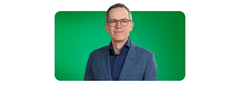 Derek Rodenhausen, Managing Director y Partner de Boston Consulting Group, aparece sobre un fondo verde. Rodenhausen tiene piel clara, cabello corto de longitud media y ojos claros. Además, lleva gafas y un blazer a cuadros sobre una camisa oscura.