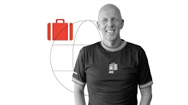 Black and white photo of Senior Vice President and Chief Marketing Officer of Booking.com, Arjan Dijk, smiling. To the left and behind him, a lifesize globe icon and a small red suitcase icon.