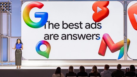 Google executive Vidhya Srinivsan speaks to an audience from the Google Marketing Live stage. A large screen behind her displays a slide from her presentation, reading “The best ads are answers.” Google logos hover around the words like balloons.