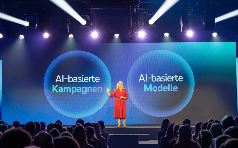 Marianne Stroehmann, Managing Director Enterprise bei Google, steht auf der Bühne der Main Show. Im Hintergrund werden auf einem großen Bildschirm die Texte „AI-basierte Kampagnen“ und „AI-basierte Modelle“ gezeigt.