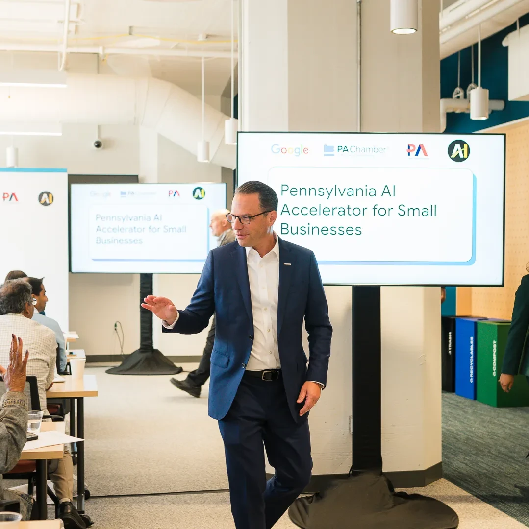Man in suit gestures at Google AI Accelerator event; woman raises hand in audience.
