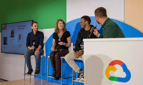 A panel of hosts is seated on a stage, engaged in a discussion.