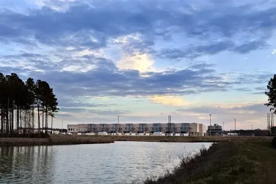 Google data center facility visible across a body of water under a cloudy sunset sky