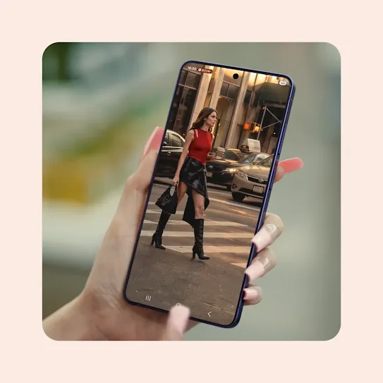 A person uses the Circle to Search feature on their Samsung Galaxy smartphone to identify an outfit in a photo. After circling the look, Circle to Search provides details and shopping links for the specific items: a Courrèges red top and a black miniskirt. The scene then cuts to a member of the K-pop group LE SSERAFIM, who is now wearing the exact same outfit while walking down a grocery store checkout as if it were a fashion runway.
