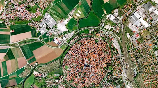 Top-down satellite view of a town featuring a distinct, densely packed circular historic center with red roofs