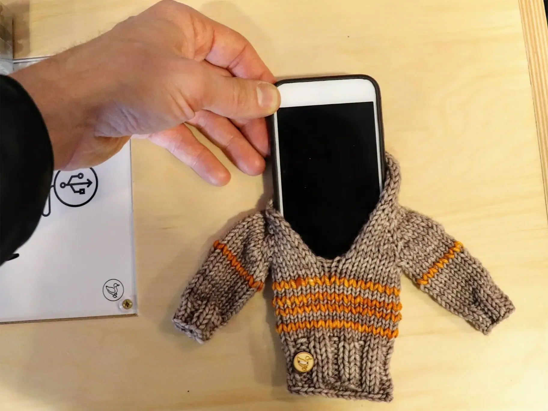 A phone with a cover that looks like a miniature version of a knitted sweater. 