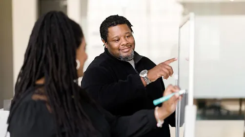 A man and a woman writing on a white board.