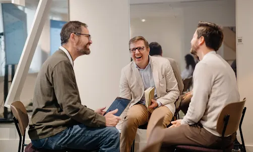 A group of three people talking, one of whom is holding a tablet device.