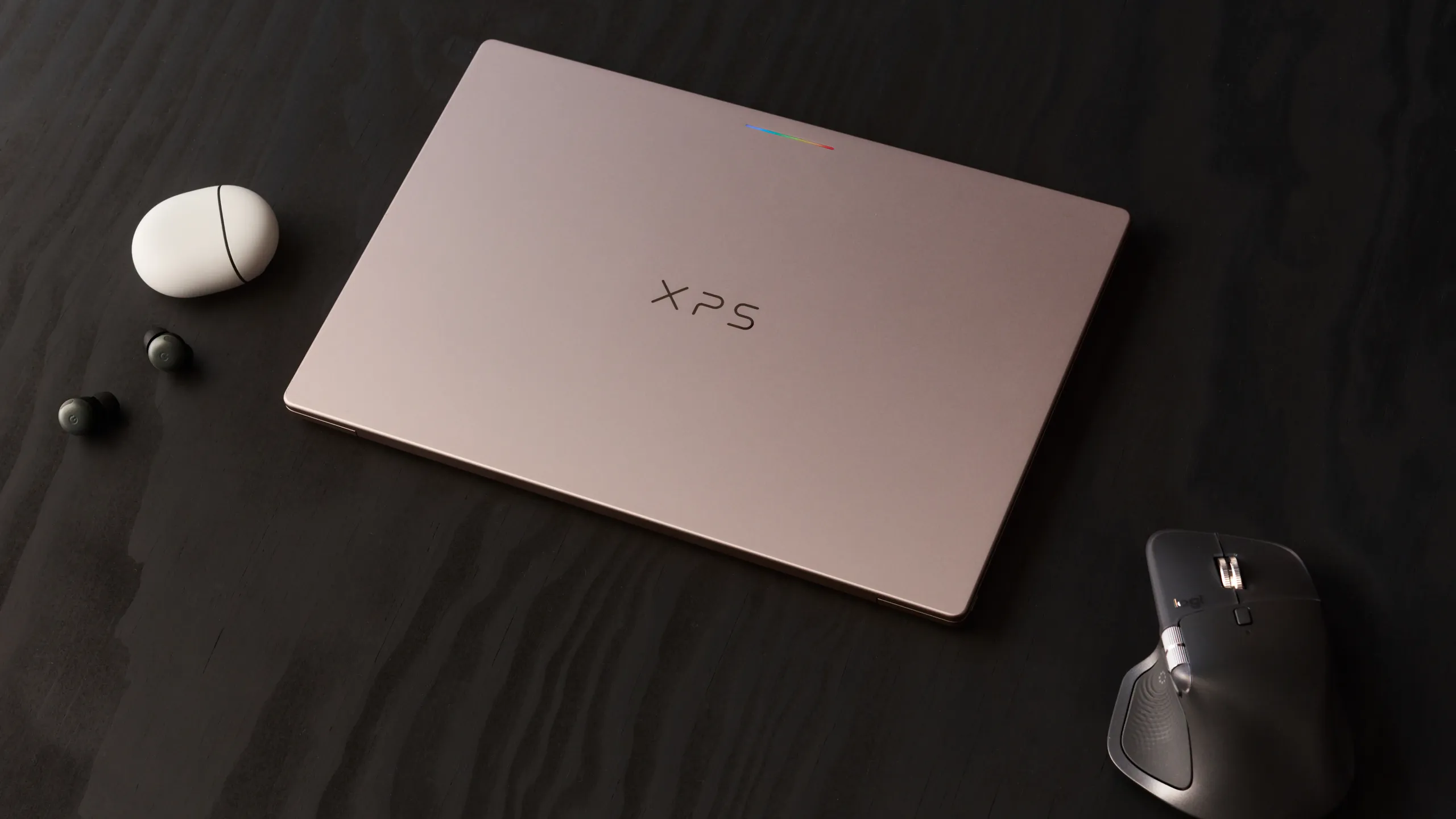 A laptop laid flat on a dark wooden surface, alongside earbuds and a computer mouse.
