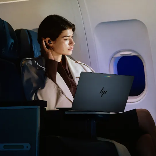 A person working on an Googlebook laptop while sitting in a business class seat on an airplane at night. They are looking out the window, and the cabin is dimly lit.