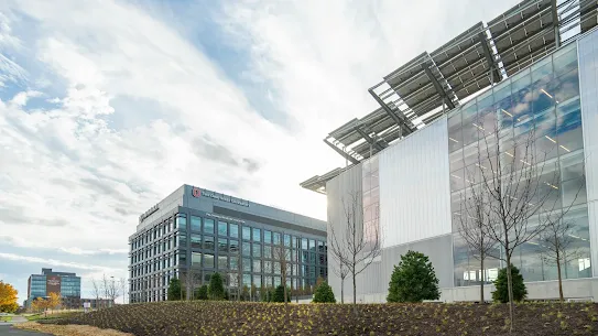 An exterior view showing two modern buildings under a cloudy sky, with solar panels mounted on top of the structure on the right