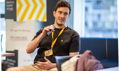 A person is seated on a stage, engaged in a discussion.