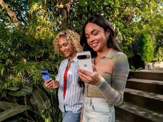 Two women using their Android devices outdoors, with trees in the background.