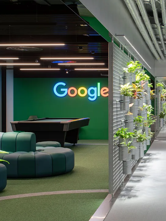 Ruang kerja dengan logo Google, sofa, dan tanaman.