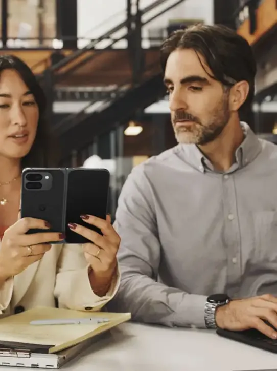 Mulher mostrando algo na tela de seu smartphone para um homem em um ambiente de trabalho.