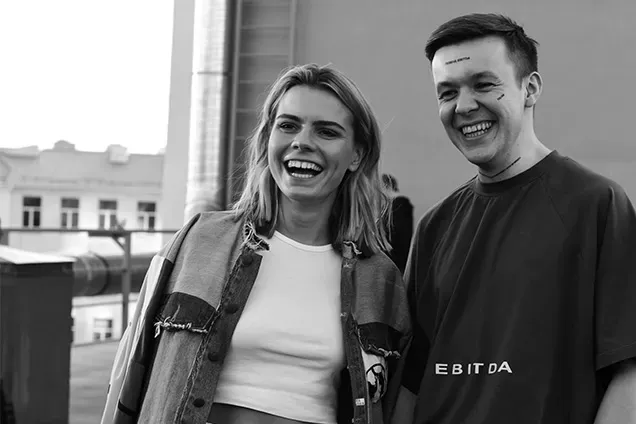 A black and white photograph of Alyona Mysko and Yaroslav Azhnyuk, the co-founders of Fuelfinance, laughing together outdoors. Yaroslav is wearing a t-shirt with "EBITDA" printed on it, symbolizing their work in financial technology and startup growth.