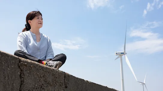 Googler Melody Chang sits on a wall with a windmill in the background in Changhua County Taiwan