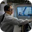 A female scientist wearing a white lab coat and protective safety glasses working with high-tech equipment in a laboratory. She is focused on a task near a machine with a blue-rimmed viewing window.