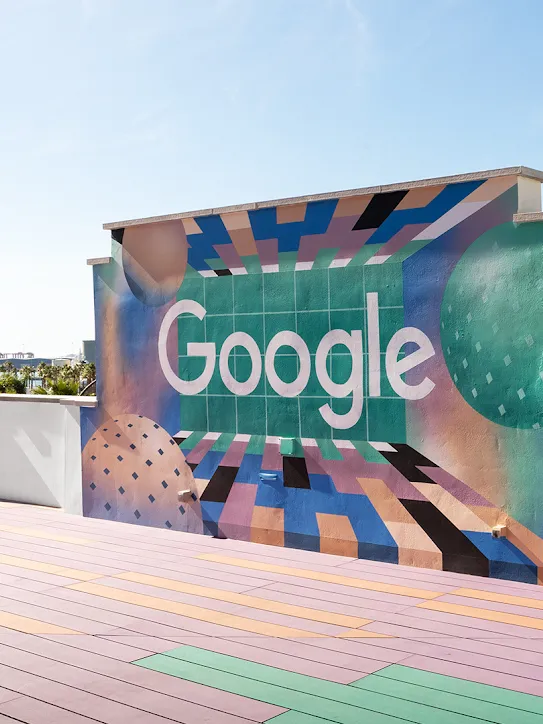 옥상에 있는 벽에 Google 로고가 있습니다. 멀리 야자수와 배가 보입니다.