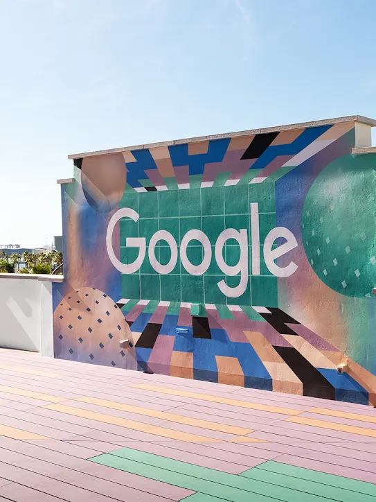 牆上有 Google 標誌的屋頂。遠處有棕櫚樹和船隻。