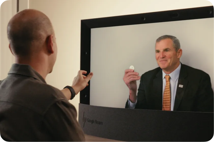 A person holds up a coin to illustrate the life-like 3D capabilities of Google Beam.