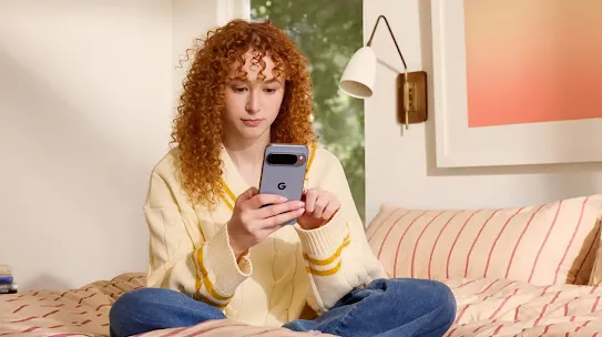 A woman sitting on a bed and using a smartphone with both hands.