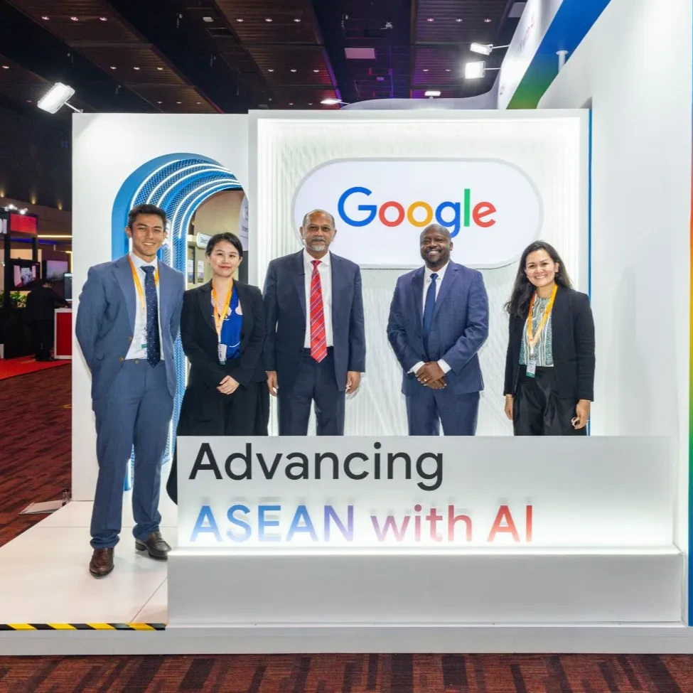 A group of people in business clothes smile and pose with a Google booth and the sign Advancing ASEAN with AI