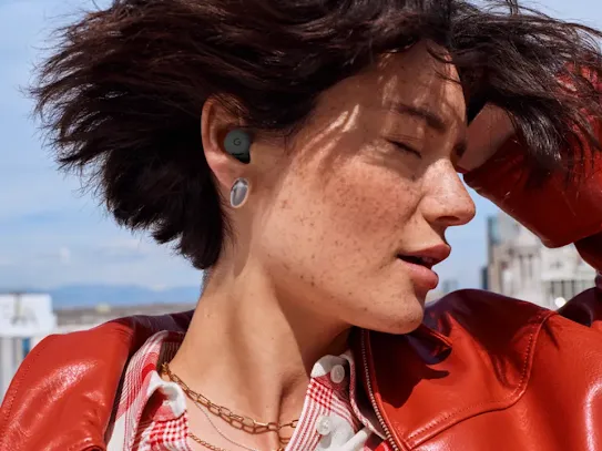 Woman using earbuds with a blue sky and a city skyline in the background.
