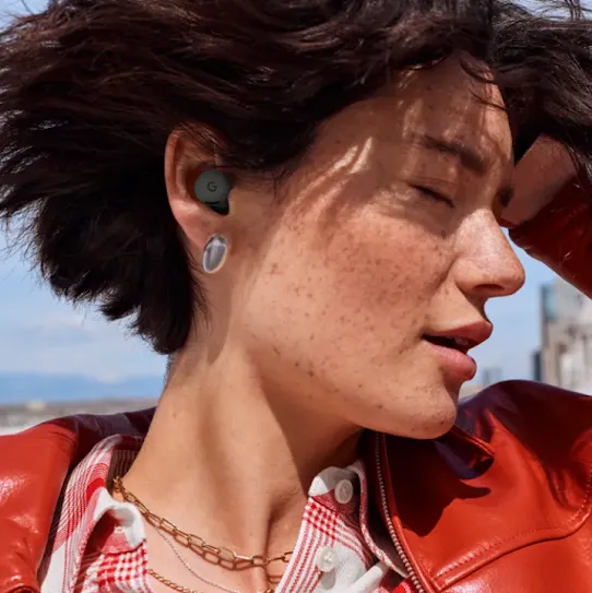 Woman using earbuds with a blue sky and a city skyline in the background.
