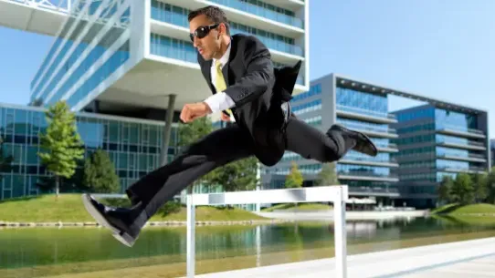 person in business suit leading over a hurdle in front of business offices