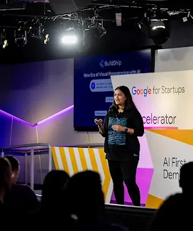 A lady on the event stage is addressing the audience while holding microphones.
