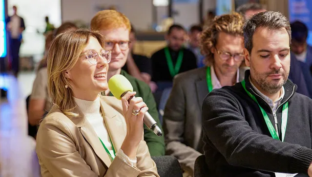 A woman sits with some people and holds the mic in hand.