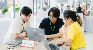 Three people seated around a laptop, collaborating and looking at the screen.