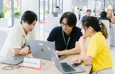Three people seated around a laptop, collaborating and looking at the screen.