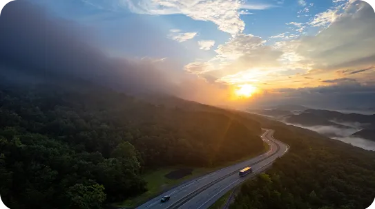 winding highway around mountains with sunset in the distance.