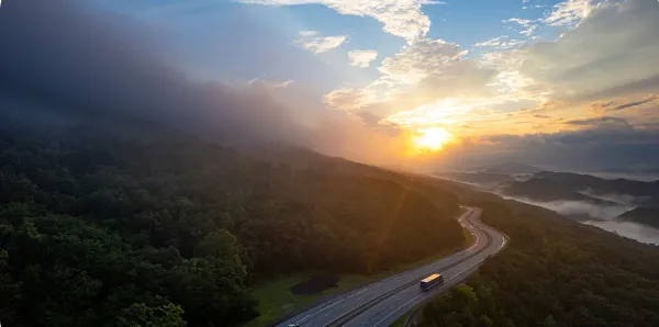 winding highway around mountains with sunset in the distance.