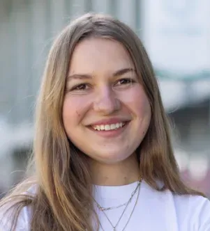 Close-up portrait of Chiara "ChiChi" Munzi, founder of ChiChi, smiling with long light brown hair and wearing a white t-shirt and layered silver necklaces, featured in a Missouri business growth story.
