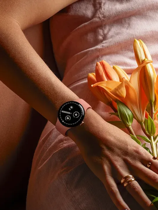 A person wearing pink clothing and a Pixel Watch holds flowers.