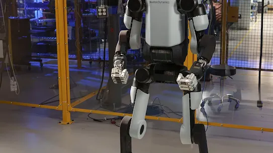 The all-electric Boston Dynamics Atlas robot stands in a laboratory setting with a glowing circular light on its head. The bipedal humanoid robot features a sleek white and black chassis. This image marks the 2026 partnership between Boston Dynamics and Google DeepMind to integrate foundational AI models into robotic hardware.